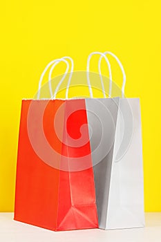 Red and grey shopping or gift bags on wooden desk against yellow background