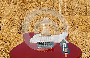 Red guitar telecaster on a straw stack background in a summer day