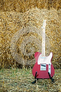 Red guitar telecaster on a straw stack background in a summer day