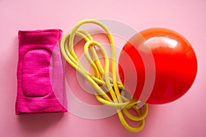 Red gymnastic ball, kneepads and skipping rope on a pink background. Sport, hobby and lifestyle concept. Top view .