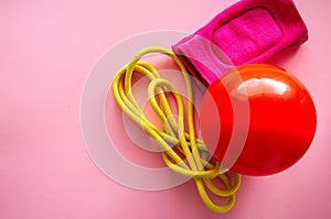 Red gymnastic ball, kneepads and skipping rope on a pink background. Sport, hobby and lifestyle concept. Top view and copy space.