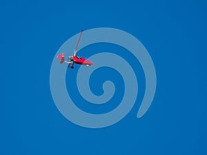 Red gyroplane flies in the blue cloudless sky photo