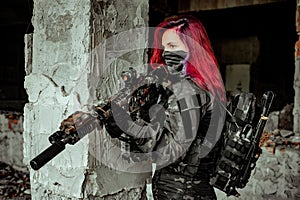 Red-hair airsoft woman in uniform with machine gun stand beside column. Closeup soldier stand inside of broken building photo