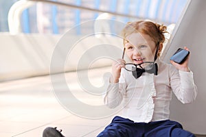 Red hair little cute girl with cell phone sits on