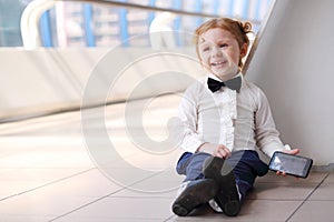 Red hair little cute girl with cell phone sits on
