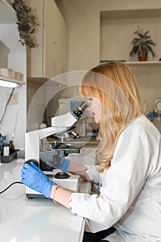 Red hair woman lab technician looking through microscope analyse blood