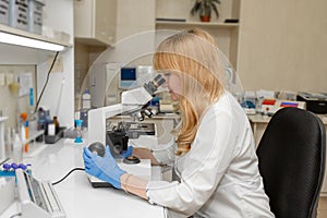 Red hair woman lab technician looking through microscope analyse blood