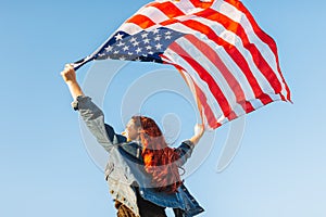 Red hair young woman standing facing the sky with her hands holding usa flag for freedom concept. 4th of July, Independence day