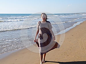 A red-haired barefoot teenage girl walks along the seashore along the water`s edge