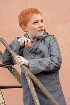 Red-haired boy in a grey coat climbed the rusty metal ladder to