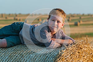 The red-haired boy lies on top of a straw bale on a wheat field
