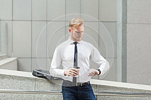 Red haired businessman looking at smart watch and holding cup.