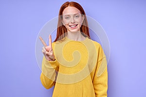 red-haired caucasian woman looking at camera showing victory gesture