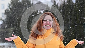Red-haired Caucasian woman rejoices in winter and catches snowflakes with her palms.