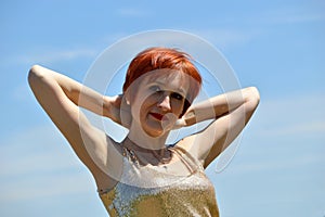 Red-haired cheerful woman smiling and looking at camera. She touching her hair with hands . Enjoying freedom and rest on a summer