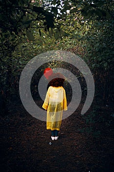 Woman in a yellow raincoat holding a red balloon on the background of forest.