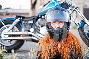 Red-haired curly woman in a helmet near a motorcycle.