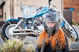Red-haired curly woman in a helmet near a motorcycle.