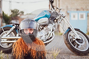 Red-haired curly woman in a helmet near a motorcycle.