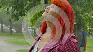 Red-haired girl becomes wet under the rain.
