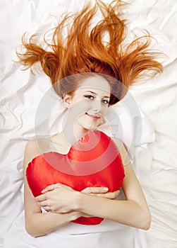 Red-haired girl in bed with toy heart.