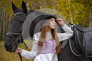 Red-haired girl in a black hat with a horse in the autumn forest.