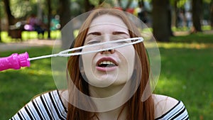 Red-haired girl blows soap bubbles in the park