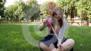 Red-haired girl blows soap bubbles in the park