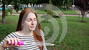 Red-haired girl blows soap bubbles in the park Slow Motion