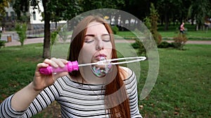 Red-haired girl blows soap bubbles in the park Slow Motion