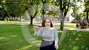 Red-haired girl blows soap bubbles in the park Slow Motion