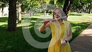 Red-haired girl blows soap bubbles in the park.yellow dress