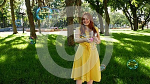 Red-haired girl blows soap bubbles in the park.yellow dress