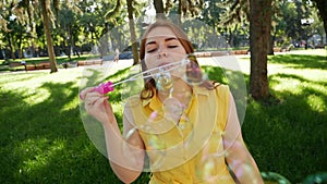 Red-haired girl blows soap bubbles in the park.yellow dress