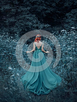 Red-haired girl in a blue, sapphire, luxurious dress in the floor, with an open back and a long train. The princess