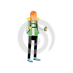 Red-haired girl in camping outfit with backpack on her shoulders standing and taking photo on smartphone. Camping or