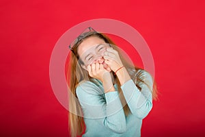 Red-haired girl covered her face with her hands, photo studio  on red background