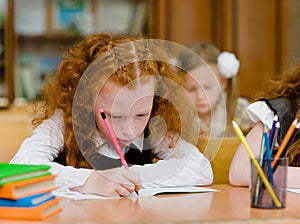 Red-haired girl drawing in copybook in classroom