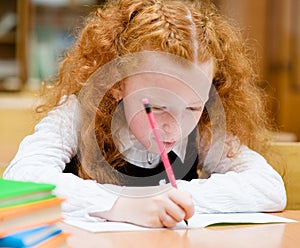 Red-haired girl drawing in copybook in classroom