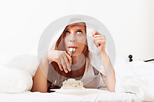 Red-haired girl eating biscuit in bed