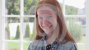 Red haired girl with freckles smiling against white window