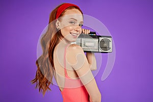 Red-haired girl with freckles stands with portable audio player, looks playfully in camera