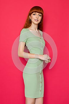 Red haired girl in green fitted dress on red background