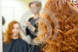 The red-haired girl in hairdresser s makes hairstyle