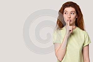 Red-haired girl keep finger at lips tell about sale