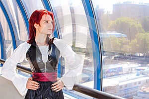 Red-haired girl in a long dress walks on the bridge