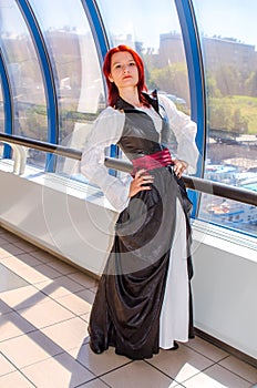 Red-haired girl in a long dress walks on the bridge