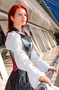 Red-haired girl in a long dress walks on the bridge