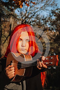 Red-haired girl with long hair plays on the ukulele in the park. School, music education concept, student learns to play the