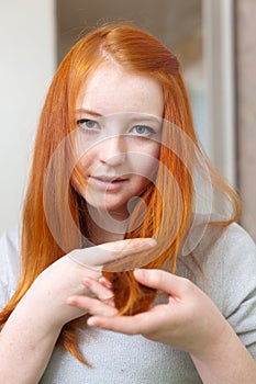 Red-haired girl looks at the tips of hair